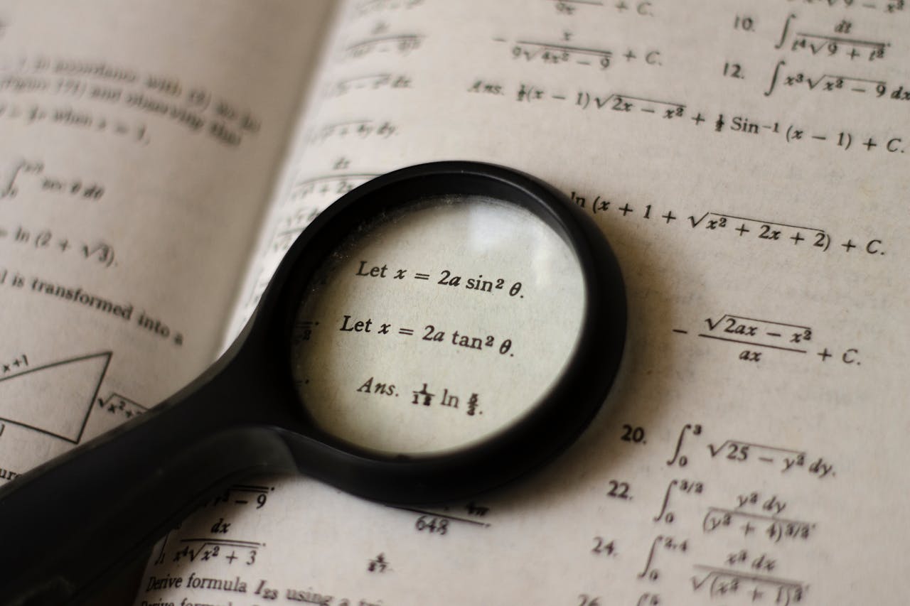 Home A magnifying glass focusing on mathematical equations in a textbook, symbolizing detailed study.