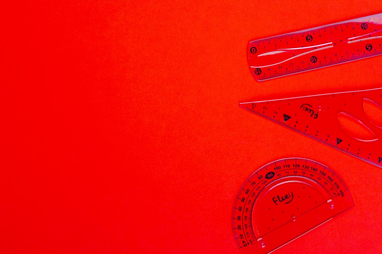 Red transparent rulers, set square, and protractor on vivid red background, ideal for educational and design content.