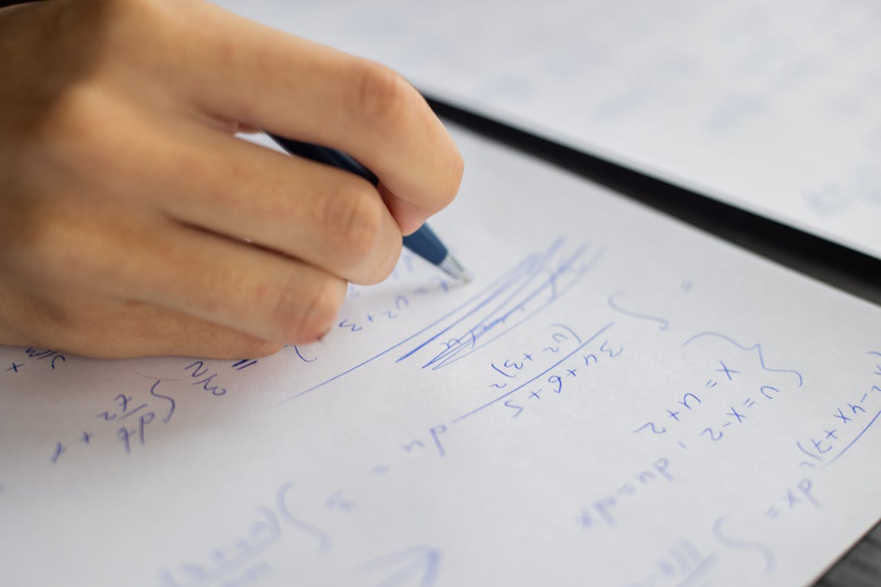 Home Unrecognizable smart student taking notes on piece of paper while solving mathematical formulas during lesson in classroom on blurred background