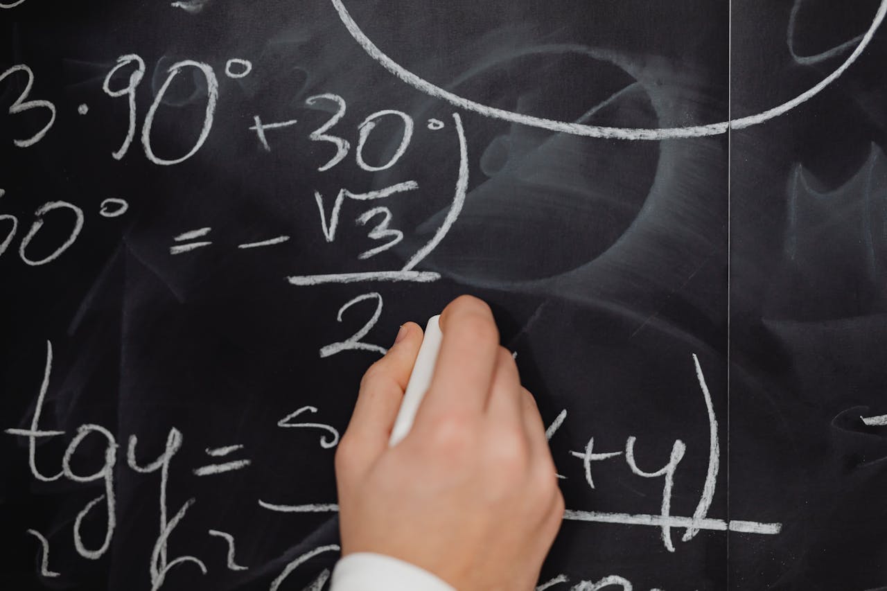 Home A hand vividly writing complex mathematical equations on a chalkboard.