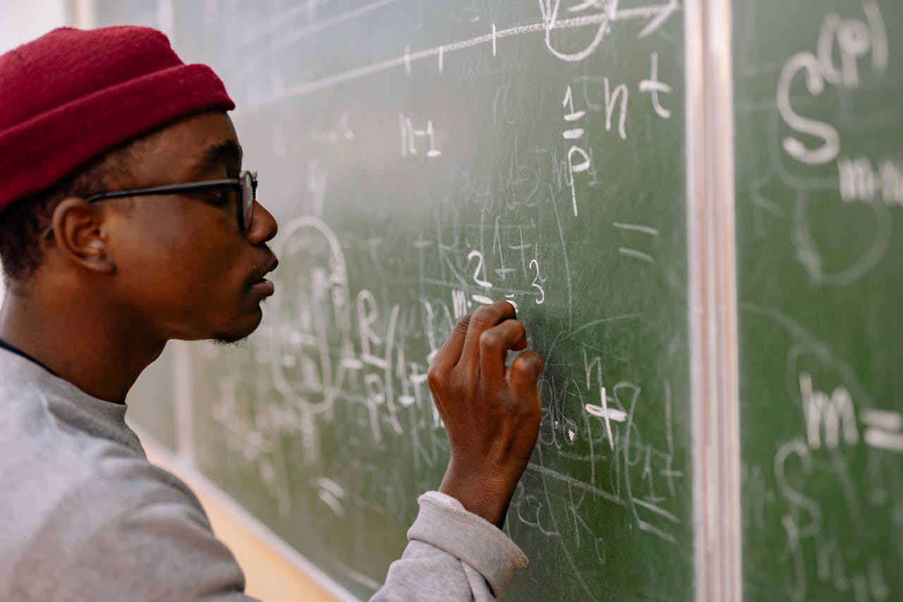 The Art of Drawing Readers In: Your attractive post title goes here A young man with eyeglasses and a red beanie solving math problems on a chalkboard.